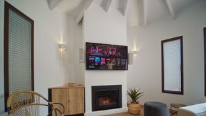 A living room with a fireplace, a television mounted on the wall, a wicker chair, and a sofa.
