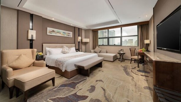 A hotel room with a large bed, a sofa, a chair, a small table with a lamp, and a TV. - Nanning Guiwanyi Hotel (Beihu South Road Subway Station) (Nanning)
