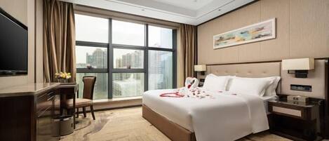 A hotel room with a large bed, a desk with a chair, a television, and a window with curtains.