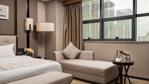 A hotel room with a bed, a sofa, a small table with a lamp, and a window with a view of high-rise buildings. - Nanning Guiwanyi Hotel (Beihu South Road Subway Station) (Nanning)