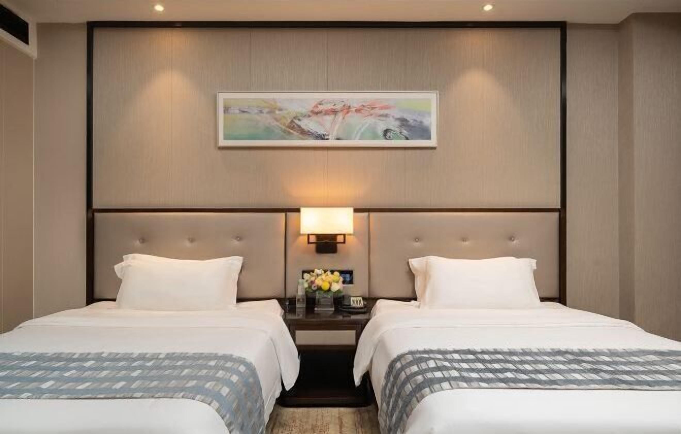 A hotel room with two beds, a nightstand with a lamp, and a painting on the wall.