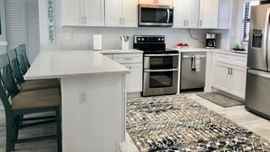 A modern kitchen with white cabinets, stainless steel appliances, a central island, and a patterned rug. - Ocean Front Luxury #801 (Cape Canaveral)