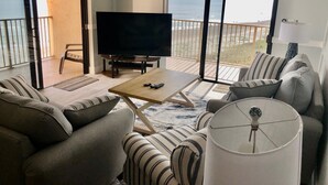 A living room with a large TV, sofas, a coffee table, and a view of the ocean through large sliding doors. - Ocean Front Luxury #801 (Cape Canaveral)