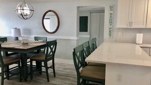 A modern kitchen with a central island, dark green chairs, and a hanging light fixture. - Ocean Front Luxury #801 (Cape Canaveral)