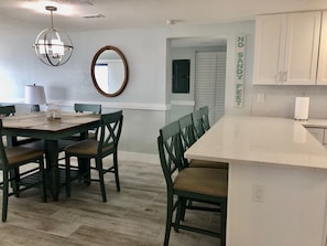 A modern kitchen with a central island, dark green chairs, and a hanging light fixture. - Ocean Front Luxury #801 (Cape Canaveral)