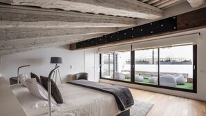 Un dormitorio moderno con una cama grande, un escritorio y vistas al exterior a través de amplios ventanales.