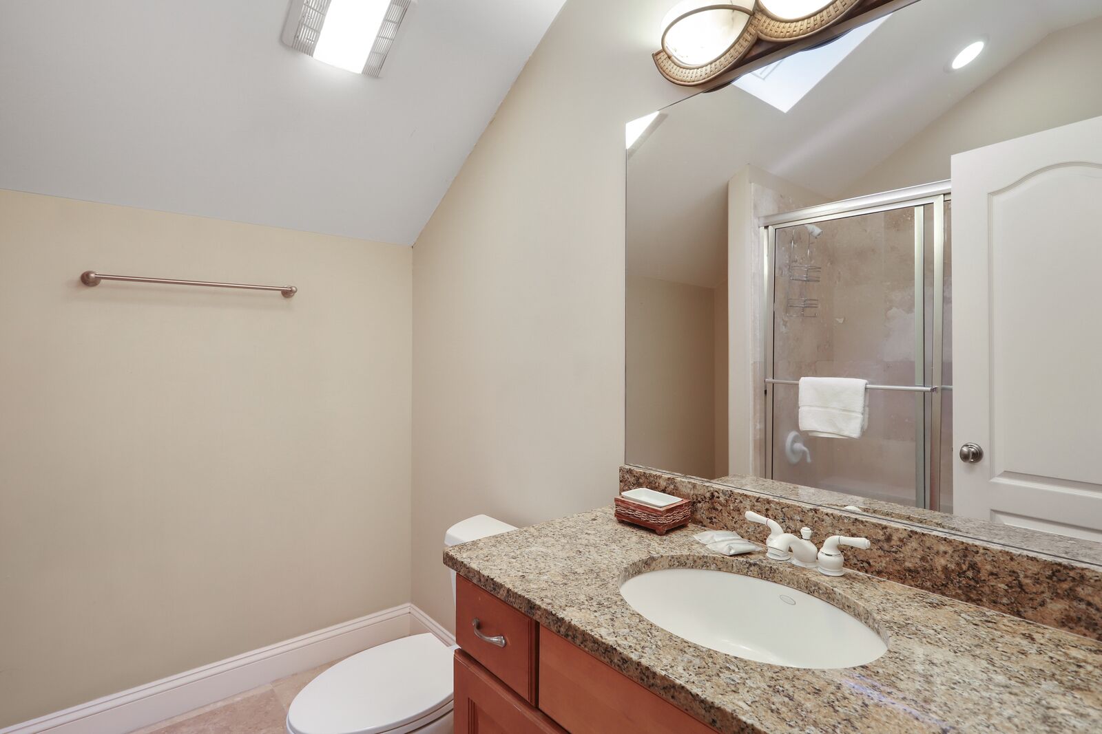 A bathroom with a granite countertop, a white sink, a mirror, and a shower enclosure.