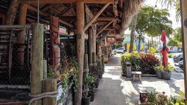 A rustic wooden structure with a thatched roof, potted plants, and a sign for 'The Coroner'. - Siesta KeyVillage heated pool (Siesta Key)