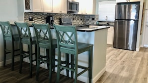 Una cocina con una isla central, taburetes de bar, un refrigerador de acero inoxidable y un microondas.