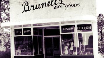 A storefront with signs for 'Hats' and 'Shoes' indicating a dry goods store.