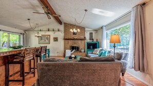 Una sala de estar acogedora con chimenea, un comedor con sillas de madera y un amplio ventanal con cortinas.