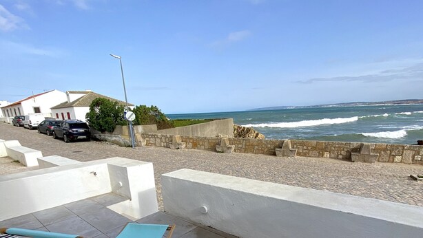 A seaside terrace with two blue lounge chairs, a stone wall, and a view of the ocean. - Baleal Waterfront (Ferrel)