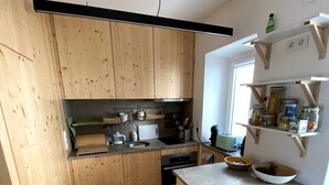 A compact kitchen with wooden cabinets, a built-in oven, and a small island with a stool. - Baleal Waterfront (Ferrel)