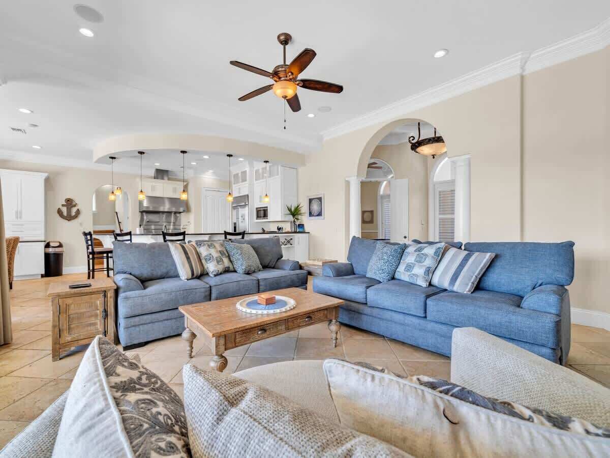 A spacious living room with a large blue sofa set, a wooden coffee table, and a ceiling fan.
