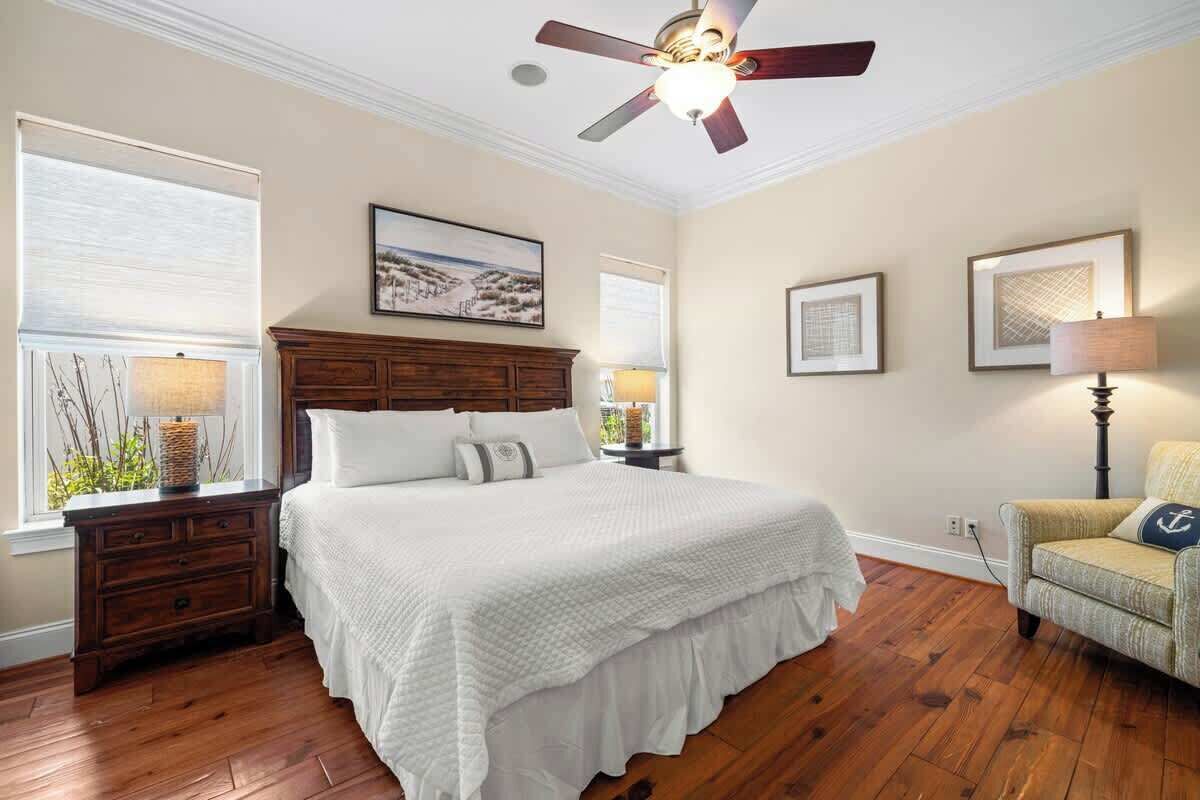 A bedroom with a large bed, wooden nightstands, a ceiling fan, and framed artwork on the walls.