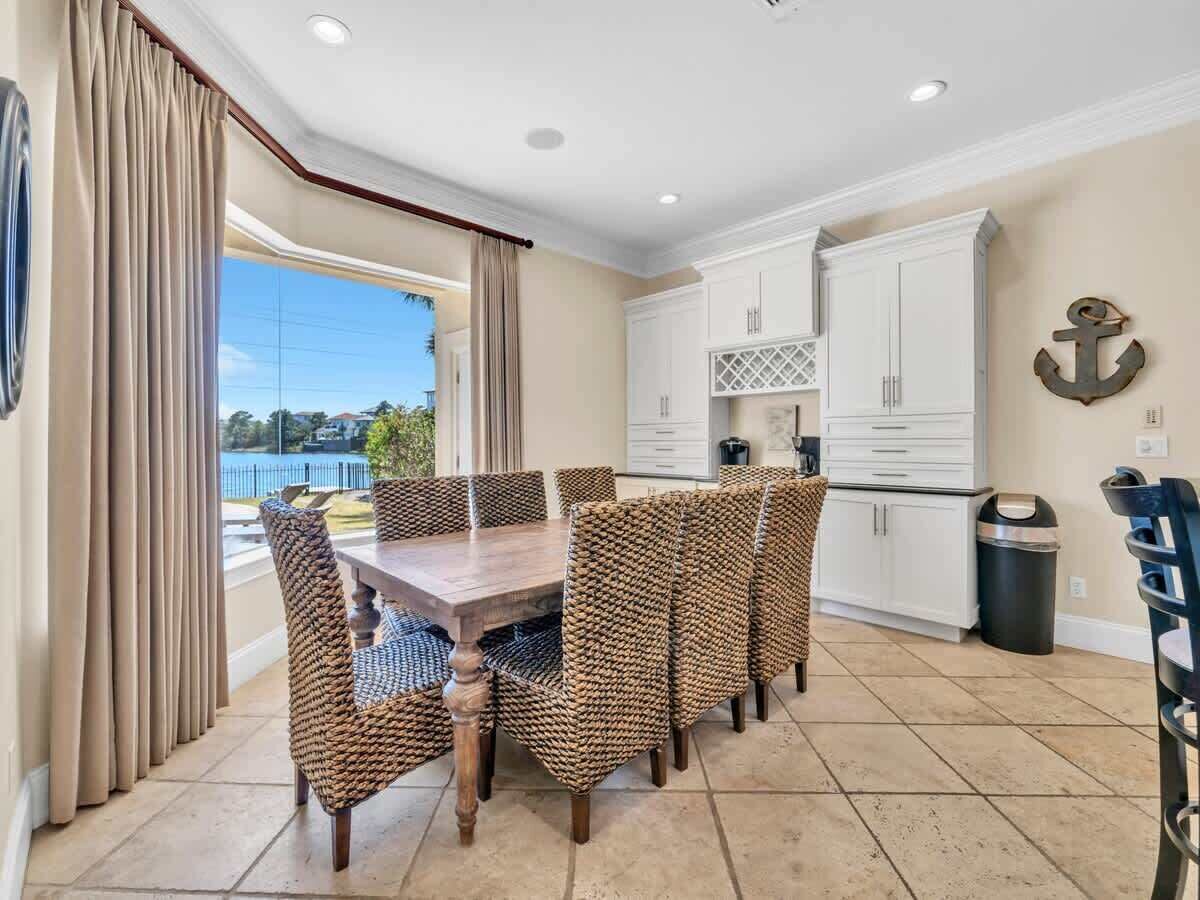 A dining area with a wooden table and wicker chairs, white cabinets, and an anchor decoration on the wall.