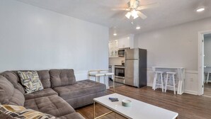 A modern living room with a sectional sofa, a white coffee table, and a kitchen area with a refrigerator, microwave, and bar stools. - 2 Bedroom Kitchen Suite#203/204 (New Smyrna Beach)