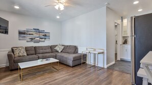 A modern living room with a grey sectional sofa, a white coffee table, and a ceiling fan. - 2 Bedroom Kitchen Suite#203/204 (New Smyrna Beach)