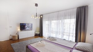 Una camera d'albergo moderna con un letto grande, una televisione, una scrivania e una finestra con tende leggere.
