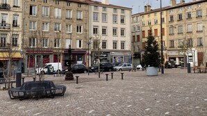 Ein Kopfsteinpflasterplatz mit einer Fontäne, Bänken und einer Reihe mehrstöckiger Gebäude mit verschiedenen Geschäften.