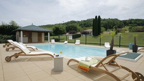 Ein Poolbereich mit Liegestühlen, einem kleinen Gebäude und einem angelegten Garten.