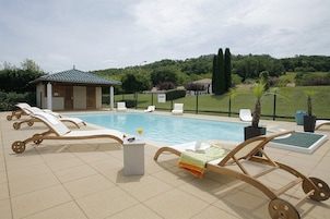 A pool area with lounge chairs, a small building, and a landscaped garden.