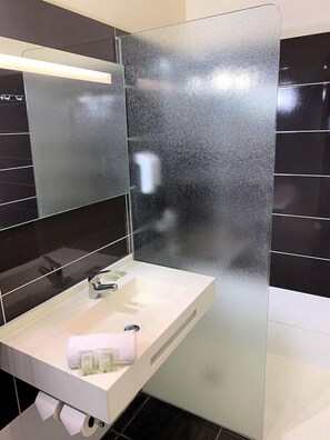 Un baño moderno con un lavamanos blanco, un espejo y paredes de azulejos negros.