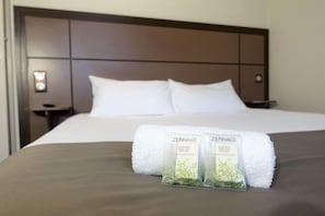 Una cama bien hecha con ropa de cama blanca y un cabecero marrón. Dos productos de baño ZENNA® están sobre la cama.