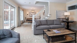 A modern living room with a grey sofa, a coffee table, and a dining area in the background. - High End Townhouse, Centrally Located, to Skiing, Mountain Biking & Rec Path (Stowe)