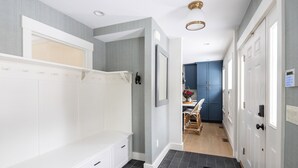 A hallway with a bench, a dining area with chairs, and a kitchen with blue cabinets. - High End Townhouse, Centrally Located, to Skiing, Mountain Biking & Rec Path (Stowe)