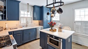A modern kitchen with blue cabinets, a central island with a built-in oven, a stainless steel range, and a hanging pot rack. - High End Townhouse, Centrally Located, to Skiing, Mountain Biking & Rec Path (Stowe)