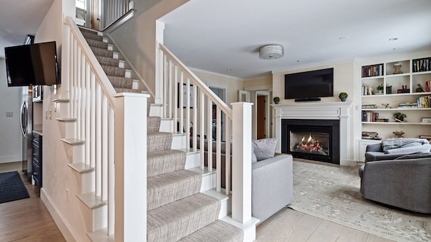 A modern living room with a staircase, a fireplace, a flat-screen TV, and a bookshelf. - High End Townhouse, Centrally Located, to Skiing, Mountain Biking & Rec Path (Stowe)