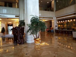 Um hall espaçoso com piso de mármore polido, uma coluna imponente e um vaso de plantas decorativo.