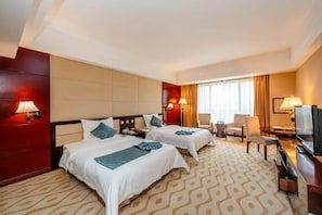 Quarto de hotel com duas camas, televisão, escrivaninha e uma cadeira.