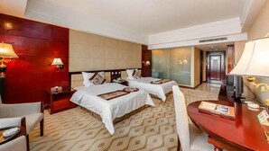 Quarto de hotel com duas camas, uma escrivaninha, uma cadeira e uma parede vermelha de destaque.