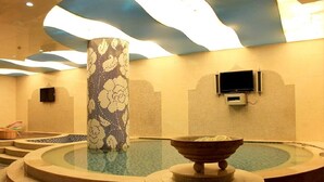 Uma área de spa com uma banheira de hidromassagem circular, um pilar decorativo e uma televisão na parede.
