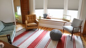 Ein gemütliches Wohnzimmer mit einem Streifenmuster-Teppich, zwei Sesseln, einer Fensterbank mit einer Pflanze und einer Holztür.