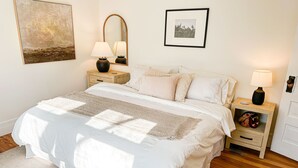 Ein ordentlich eingerichtetes Schlafzimmer mit einem großen Bett, zwei Nachttischen, einem Wandspiegel und einem kleinen Beistelltisch.
