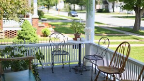 Eine Veranda mit zwei Metallstühlen, einem Holzstuhl und einem Tisch mit Topfpflanze und Vase.
