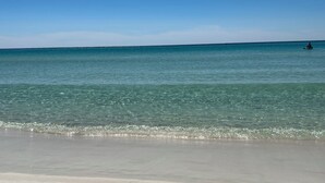 Una spiaggia con acque cristalline e una persona che pagaia in lontananza.
