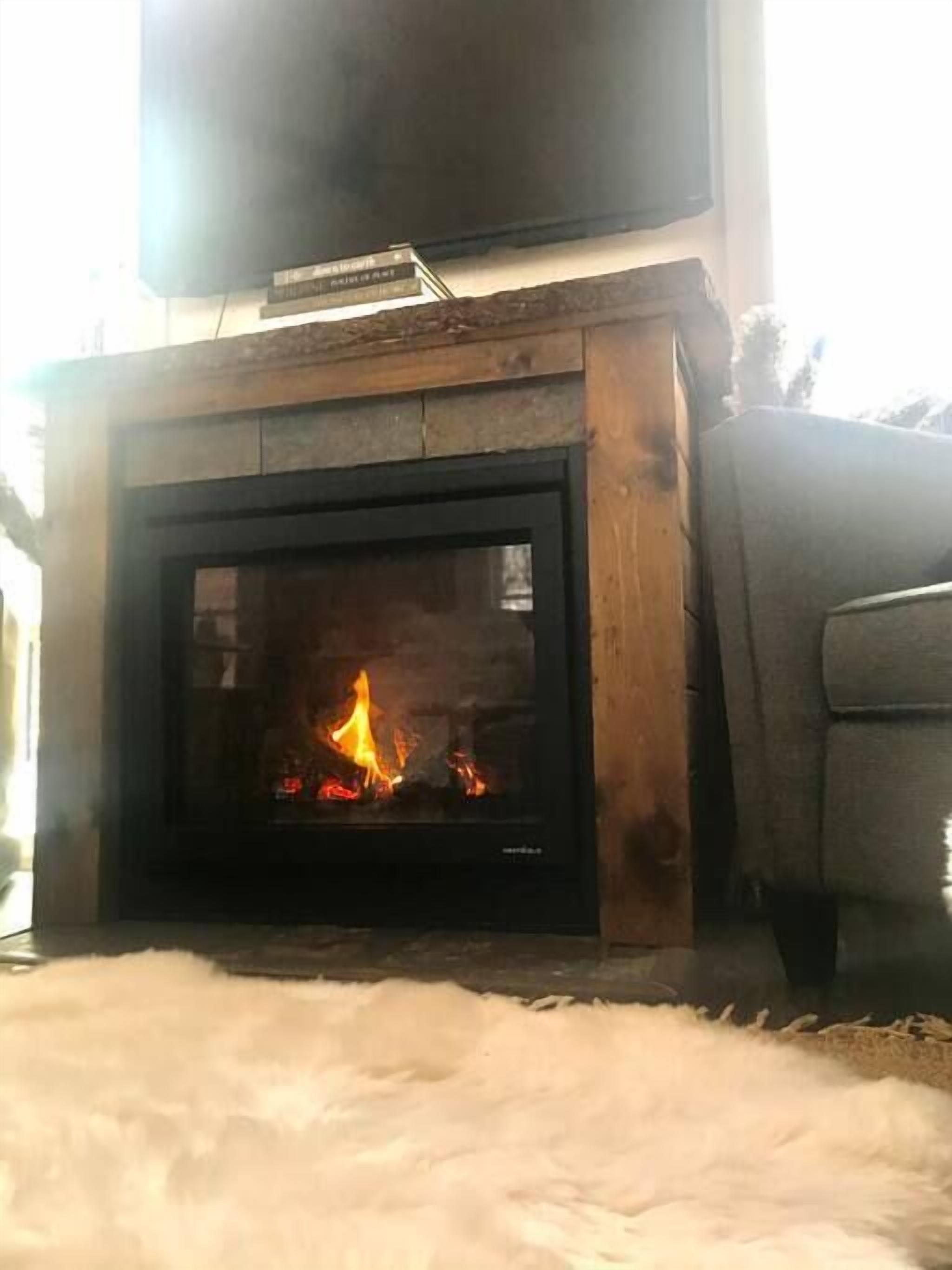 A fireplace with a TV mounted above it, a grey couch to the right, and a fluffy white rug in front.