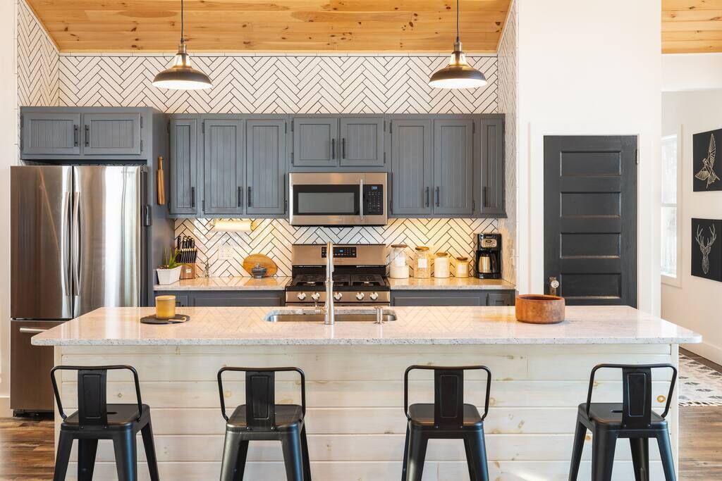 A modern kitchen with grey cabinets, stainless steel appliances, and a herringbone-patterned backsplash.