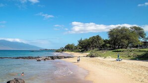 Une plage à l’eau claire, un rivage sablonneux et une montagne en arrière-plan.