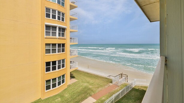 Edificio amarillo con varias ventanas y balcones que dan a una playa con olas.