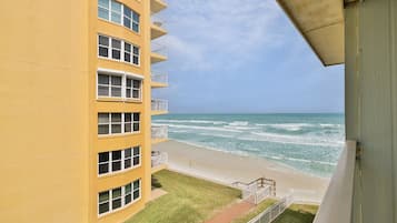 A yellow building with multiple windows and balconies overlooking a beach with waves.