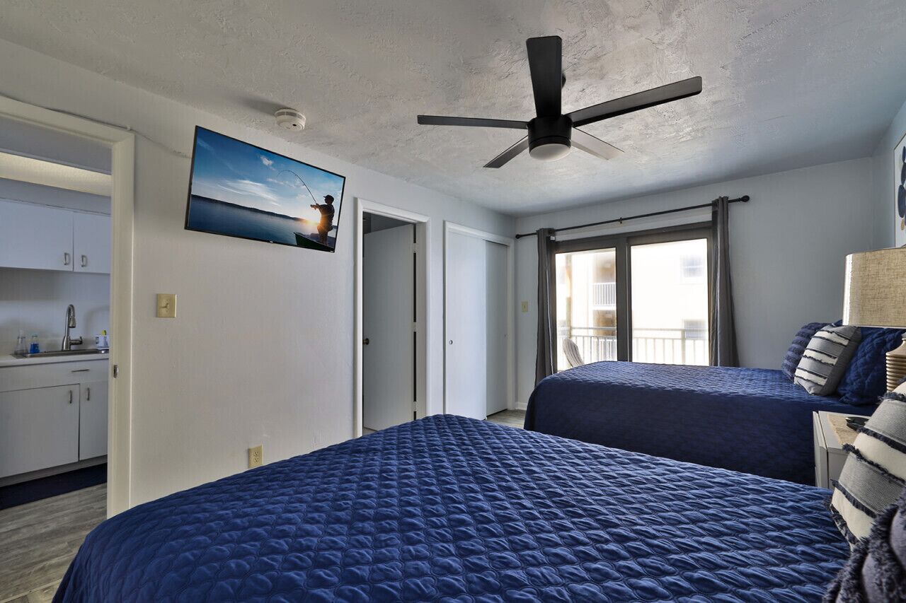 Une chambre d’hôtel avec deux lits, un ventilateur de plafond, un tableau, un balcon et une vue sur la mer.