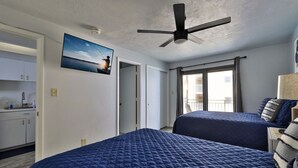 A hotel room with two beds, a ceiling fan, a painting, a balcony, and a view of the sea. - Ocean View Beach Condo #307 (New Smyrna Beach)
