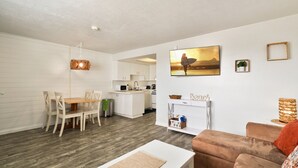 A modern living room with a dining area, kitchen, and a large window with a view. - Ocean View Beach Condo #307 (New Smyrna Beach)