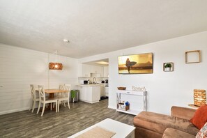 A modern living room with a dining area, kitchen, and a large window with a view. - Ocean View Beach Condo #307 (New Smyrna Beach)