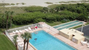 Una piscina con sillas de descanso, cancha de tenis y vista a la playa.